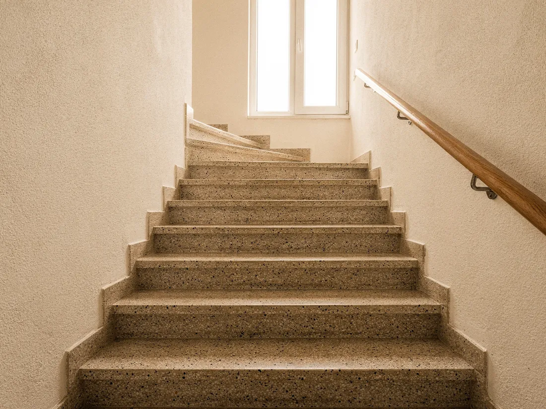 Helles, gepflegtes Treppenhaus mit Terrazzostufen und hölzernem Handlauf