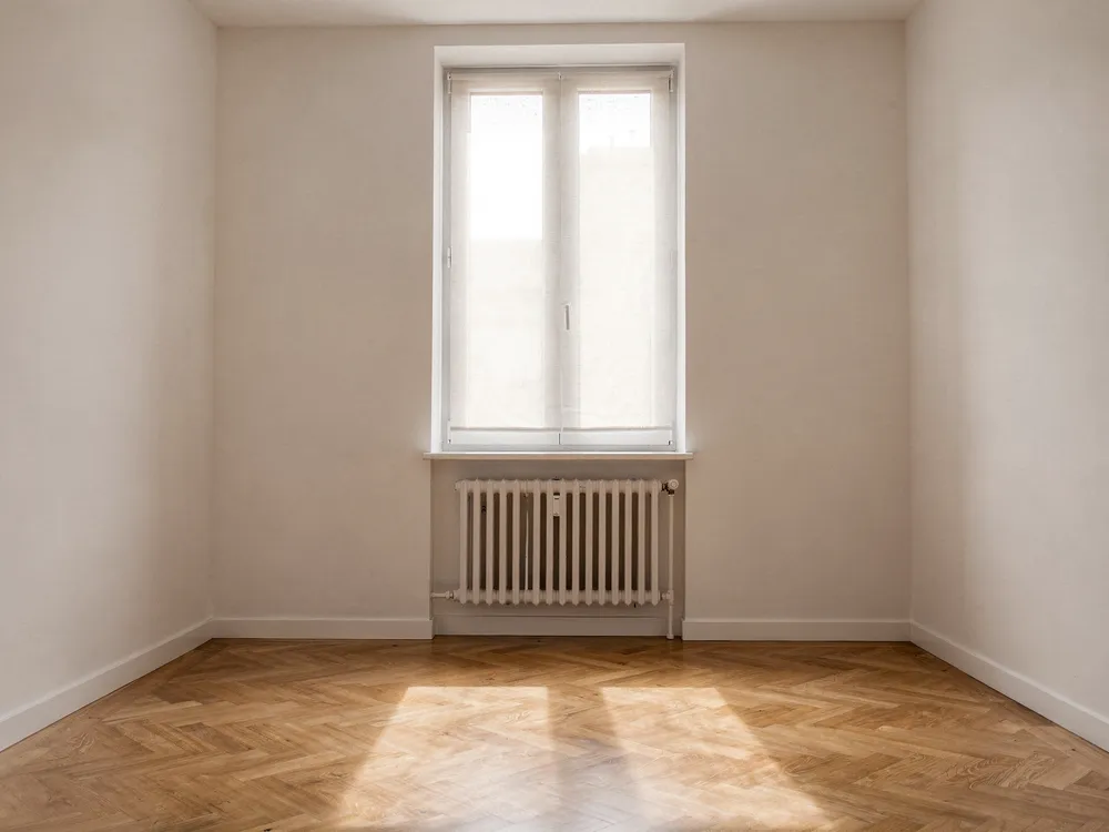 Leerer, frisch renovierter Wohnraum mit Fischgrätparkett und hohem Fenster